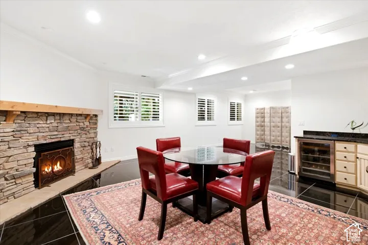 Stone-clad fireplace with wood mantle, black tile flooring, recessed lighting, white plantation shutters, and built-in wet bar with beverage cooler