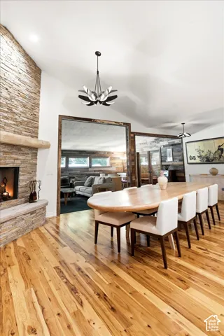 Vaulted ceiling with modern chandelier, stone-clad fireplace with mantel, and wood-finish flooring