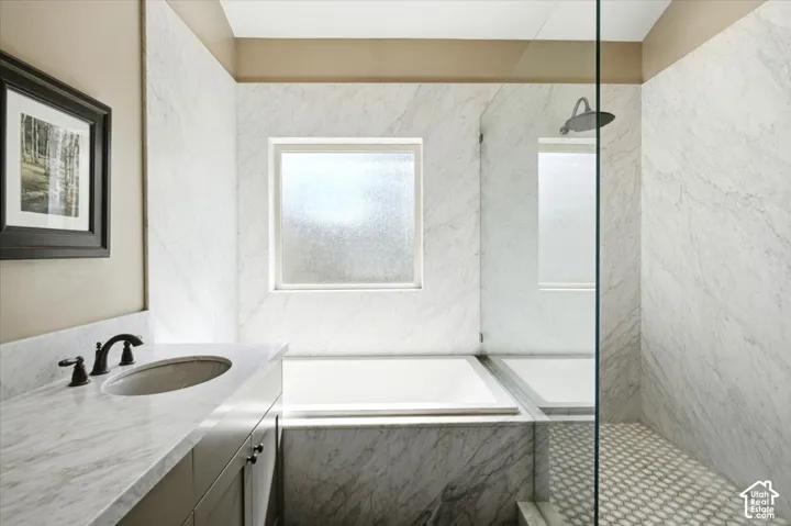 Marble-look wall tile and countertop, built-in soaking tub, glass-enclosed shower, and a single vanity with dark bronze fixtures