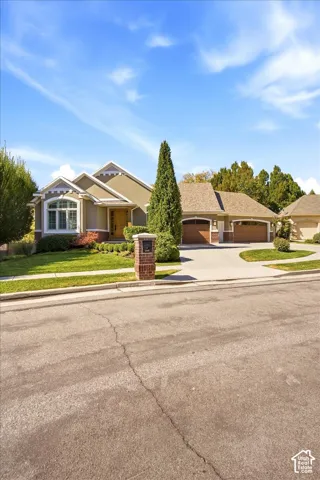 Stucco exterior featuring multiple gables, an arched window, a two-car garage with wood-finish doors, and a brick-clad mailbox