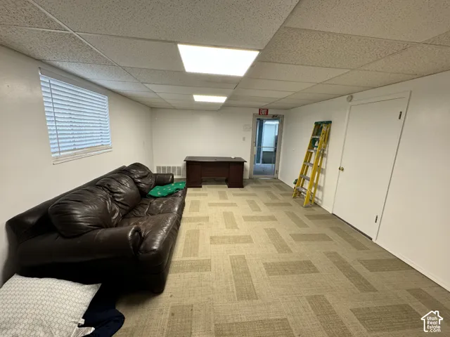 Recessed ceiling lighting, drop ceiling, window with horizontal blinds, neutral tone patterned carpet, white walls