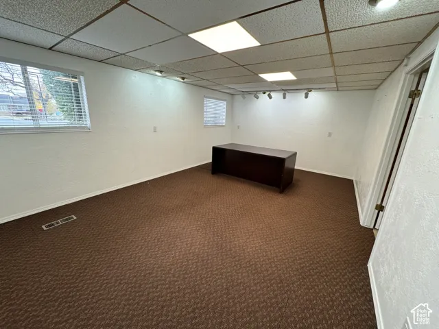 Expansive room with neutral carpeting, white walls, and a dropped ceiling with integrated lighting