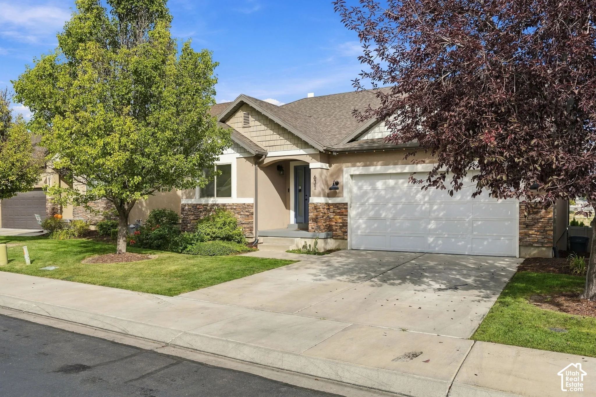 Single-story exterior featuring stucco and stone facade, an attached two-car garage, mature landscaping, and a concrete driveway