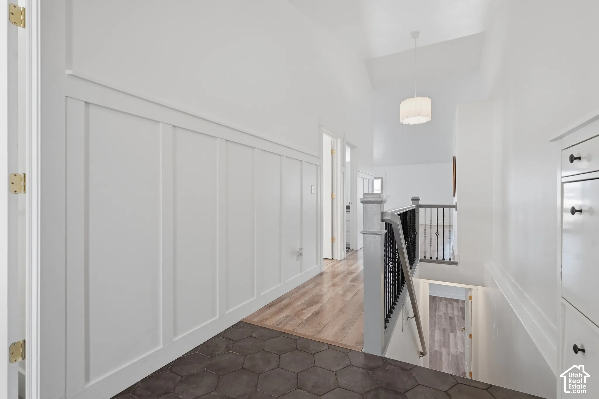 Board and batten wall paneling, hexagonal floor tiling, wood-finish flooring, black metal stair railing, and a drum pendant light fixture