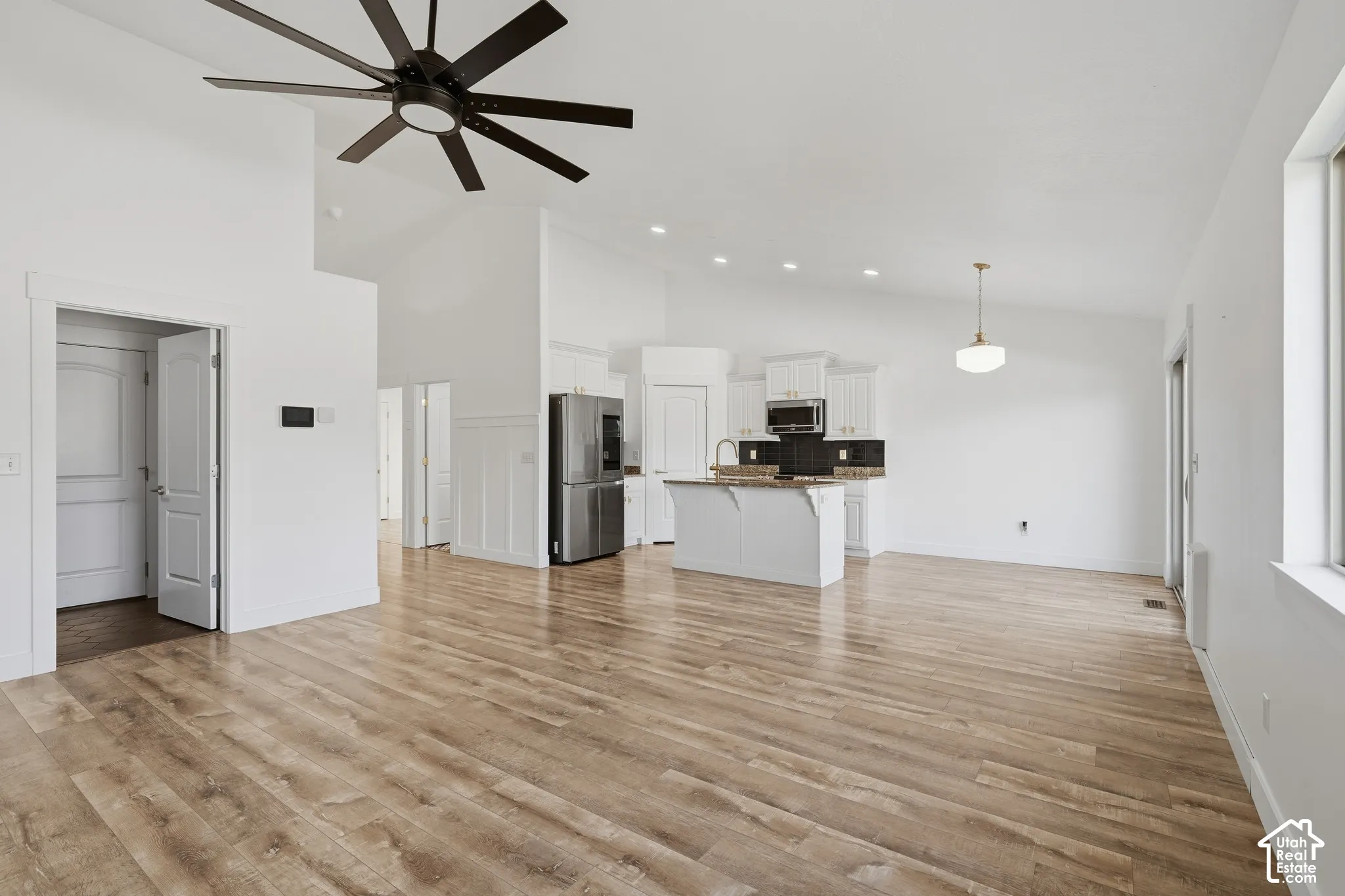 Vaulted ceiling with an oversized ceiling fan, wood-finish flooring, recessed lighting, kitchen island with seating, and stainless steel appliances