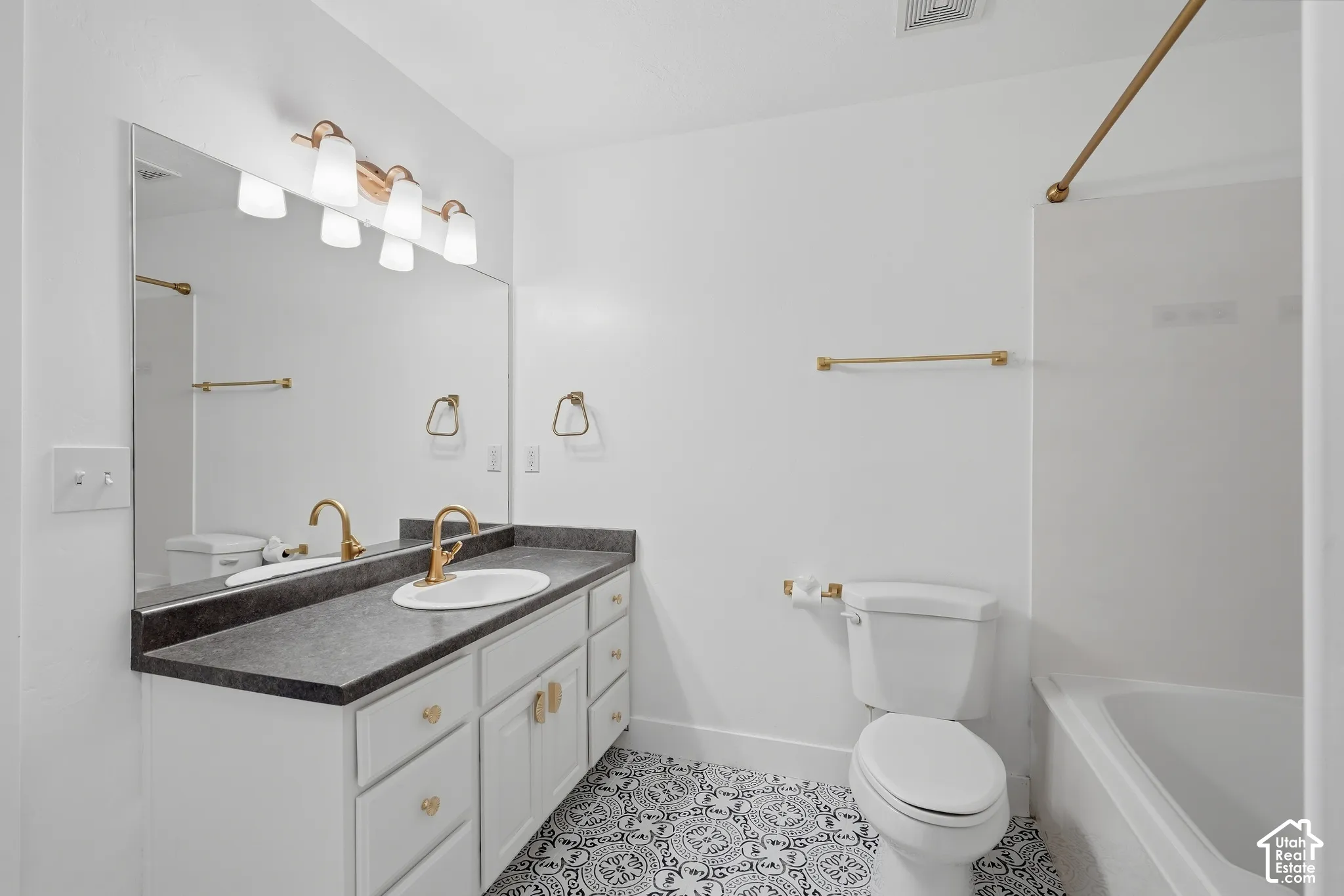 Primary / Master  bathroom featuring a double-sink vanity with white cabinetry, dark stone countertops, and brass hardware