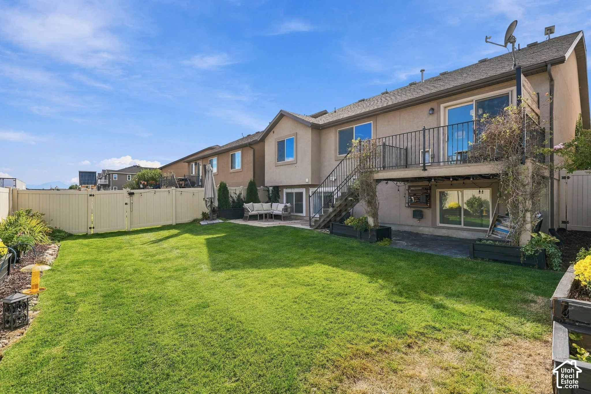 Expansive lawn area, multi-level deck with metal railings, lower-level patio, and surrounding privacy fencing