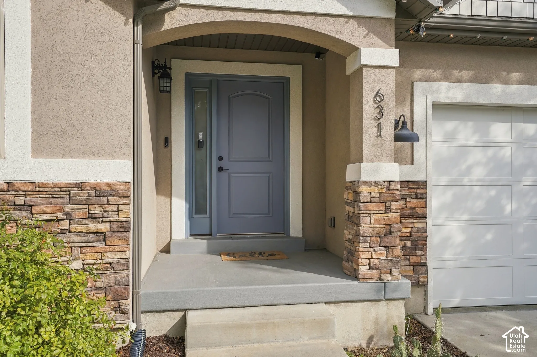 Arched entry with a paneled front door, stone veneer accents, stucco exterior, and an attached garage