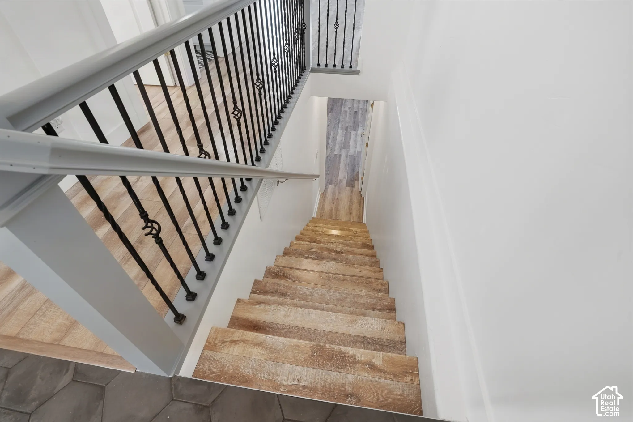 Hexagonal tile flooring, wood-finish stairs, white painted walls, wood-finish flooring, and wrought iron balusters with decorative elements