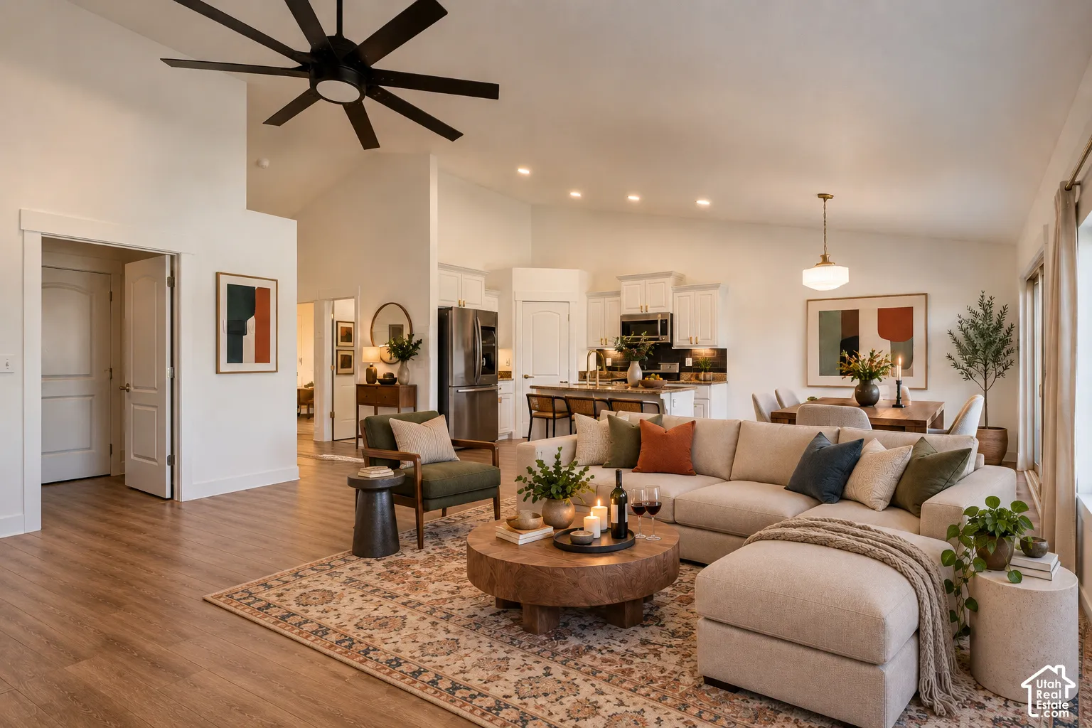 Vaulted ceilings with a large ceiling fan, wood-finish LVP flooring, granite counter and island, white cabinetry, and stainless steel appliances