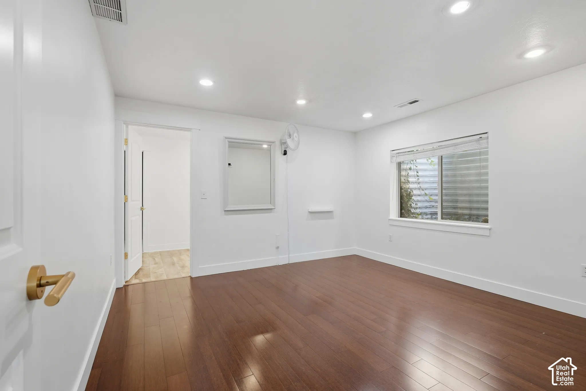 Spacious room featuring wood-finish flooring, white walls, recessed ceiling lights, and a window