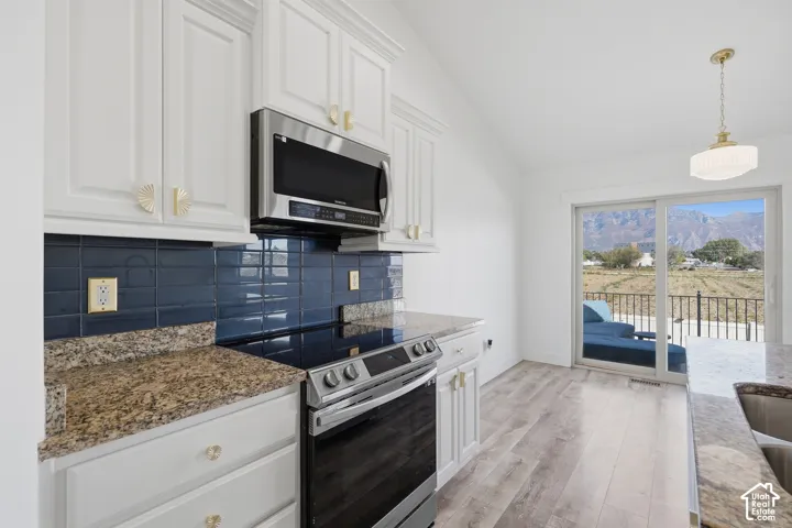 Modern kitchen featuring white cabinetry with brass hardware, stainless steel appliances including a gas range and microwave, granite countertops, and a deep navy subway tile backsplash