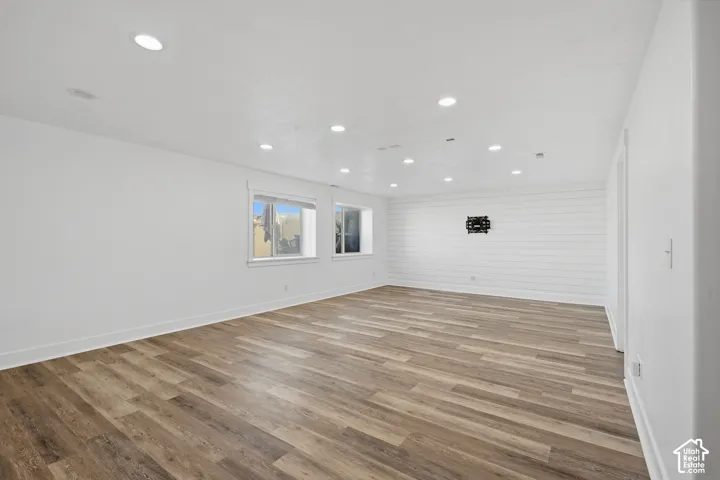 Wood-finish flooring, white walls, multiple recessed ceiling lights, horizontal paneling accent wall, and two windows