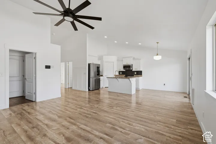 Vaulted ceiling with an oversized ceiling fan, wood-finish flooring, recessed lighting, kitchen island with seating, and stainless steel appliances