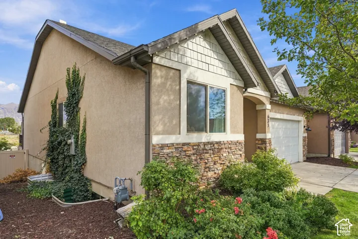 Stucco exterior with stone accent detailing, featuring a two-car garage, pitched roofline, and established landscaping