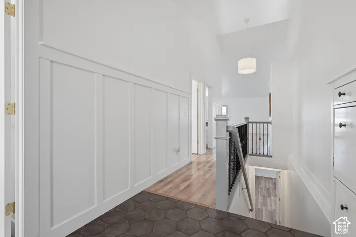 Board and batten wall paneling, hexagonal floor tiling, wood-finish flooring, black metal stair railing, and a drum pendant light fixture
