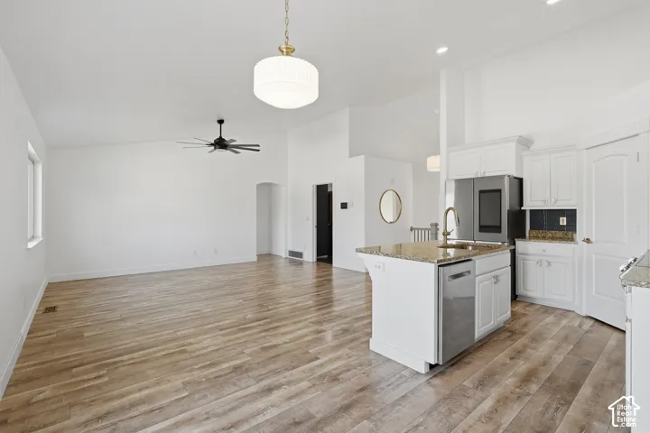 Open-concept layout featuring wood-finish flooring, vaulted ceilings, a kitchen island with built-in sink and stainless steel dishwasher, and white cabinetry