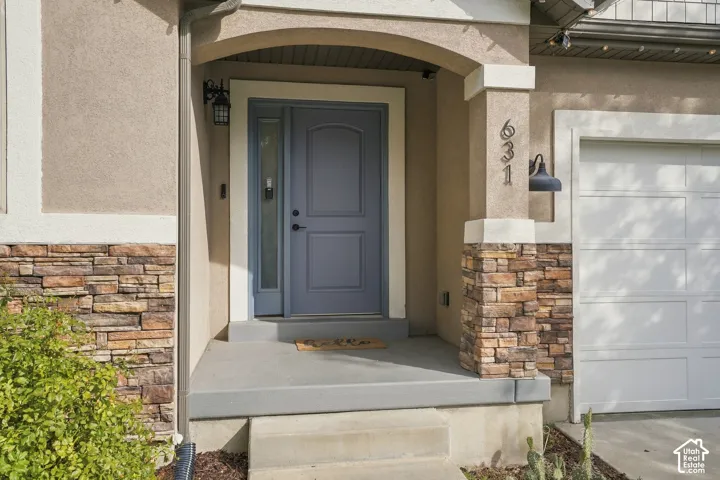 Arched entry with a paneled front door, stone veneer accents, stucco exterior, and an attached garage
