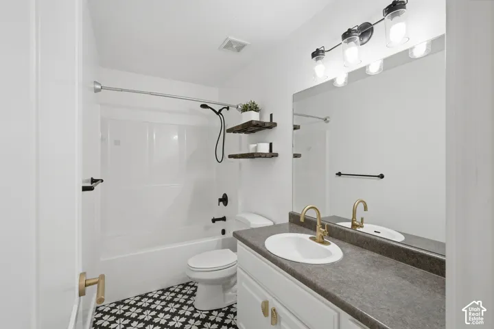 Full vanity mirror, white cabinetry, gold-finish hardware, dark countertop, and black-and-white patterned floor tile