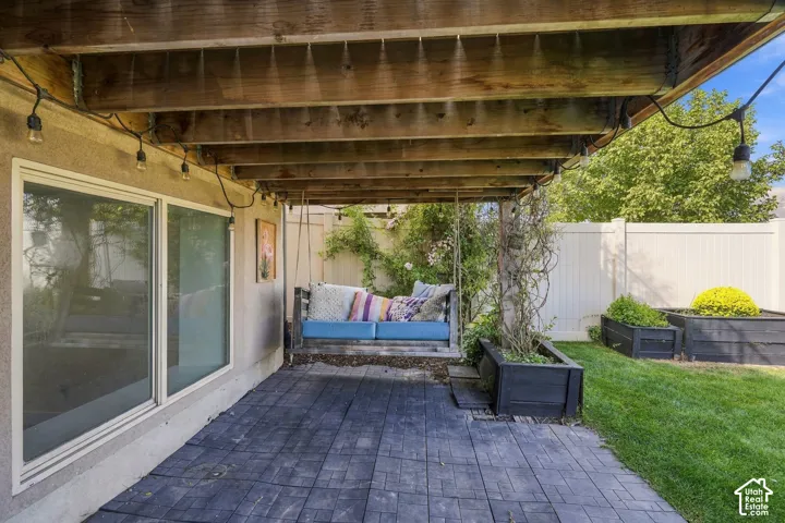 Covered patio with stamped concrete flooring, sliding glass doors, white privacy fencing, and raised garden beds