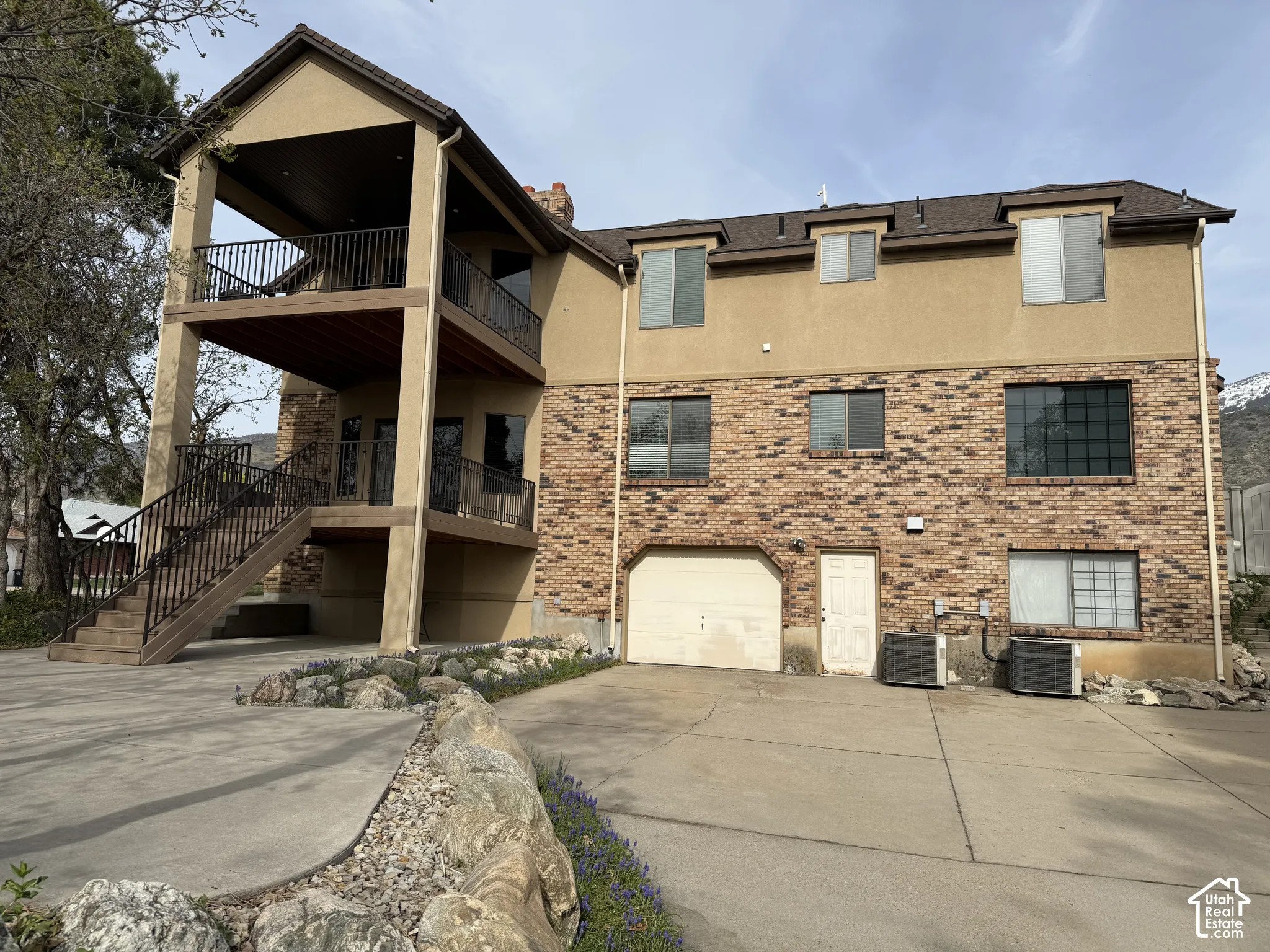 Two-story exterior with brick and stucco cladding, featuring a covered upper-level balcony and a covered lower-level patio