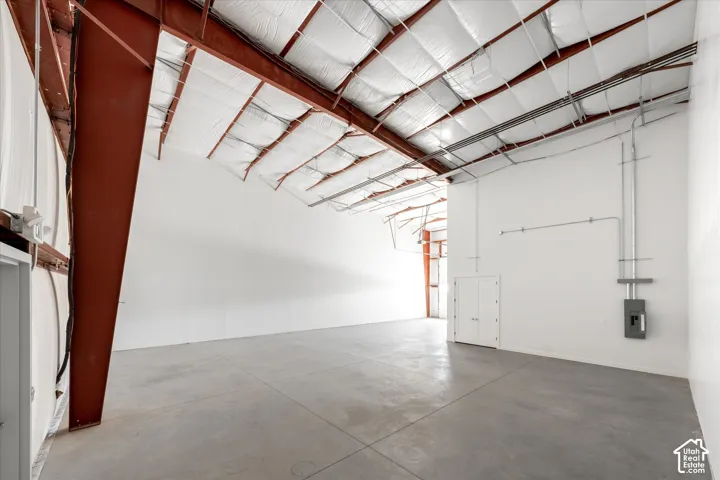 Expansive open space with concrete flooring, exposed metal structural beams, insulated ceiling, and a visible electrical panel