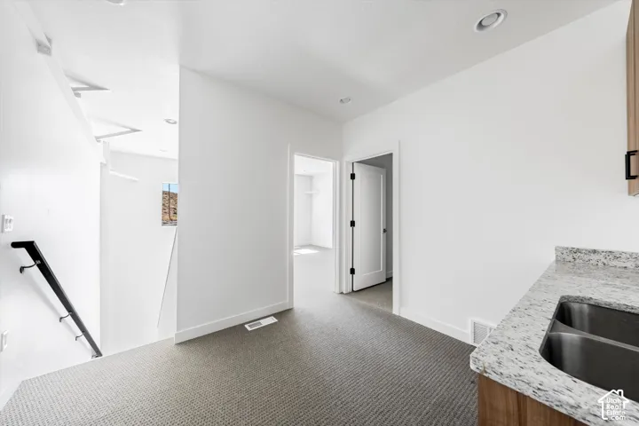 Textured carpet flooring, white walls, recessed lighting, wood-finish cabinetry, and a granite-style countertop with an undermount double sink