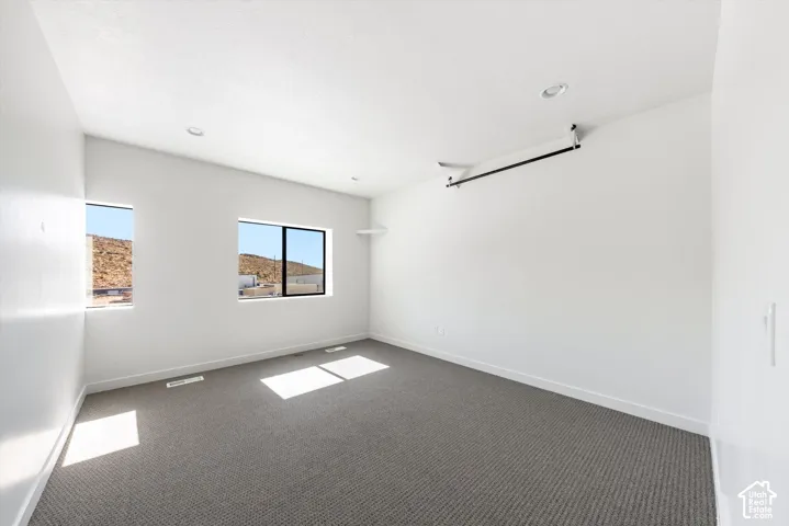 Recessed lighting, two windows, and a built-in shelf complement the light-toned walls and carpeted flooring