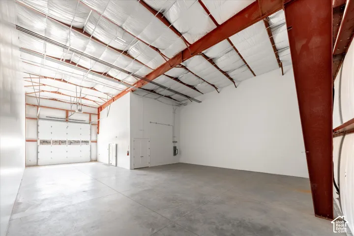 Expansive warehouse space featuring a large roll-up door, exposed structural beams, and concrete flooring