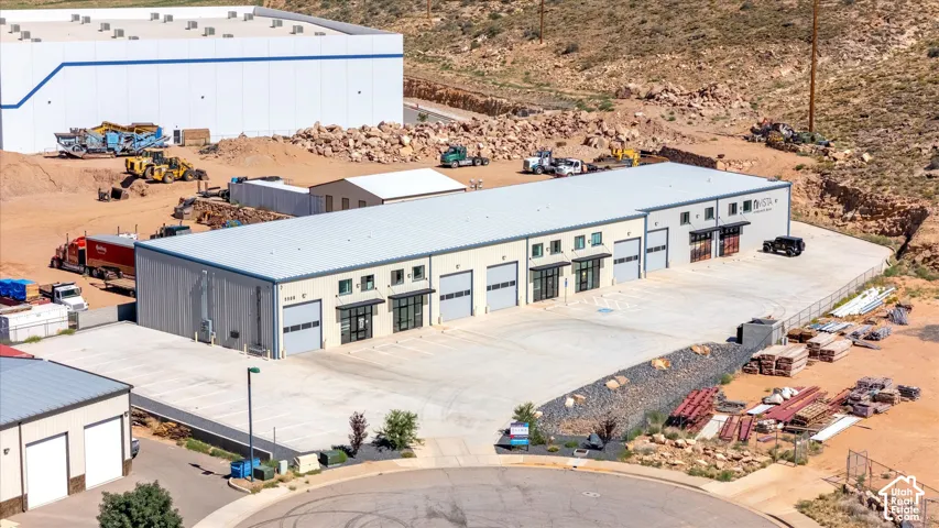Industrial building featuring multiple garage bays, an expansive paved lot, and a metal roof