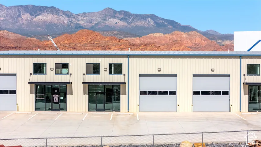 Commercial building featuring multiple roll-up doors, prominent storefront entrances, multiple windows, and a paved parking area