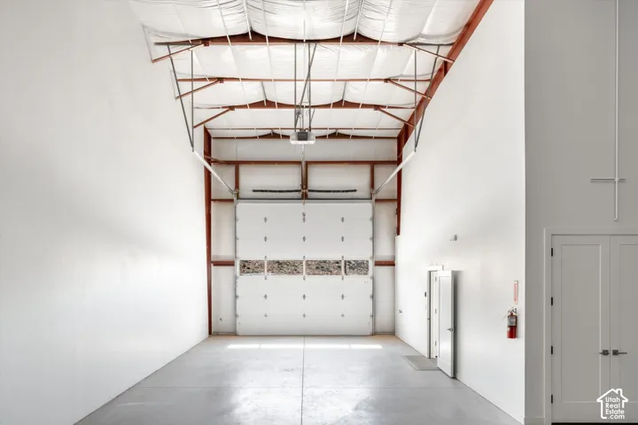 High ceilings with exposed structural beams, a large overhead door, and concrete flooring