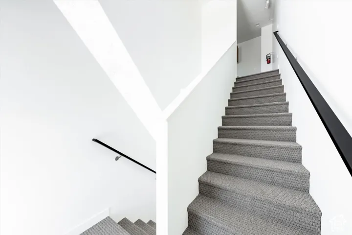 Staircase featuring grey textured carpeting and a black metal handrail