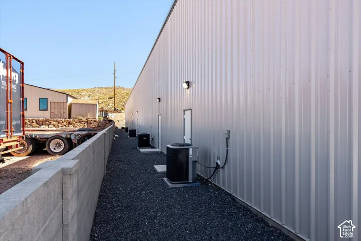 Corrugated metal siding exterior, multiple wall-mounted light fixtures, multiple HVAC units, dark gravel ground cover, and a concrete block retaining wall