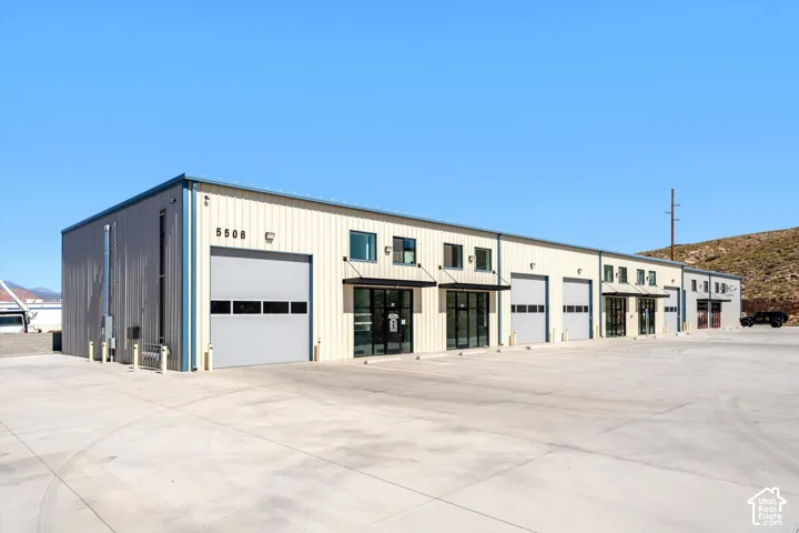 Industrial building featuring multiple roll-up doors, prominent address numbers, and a concrete parking area