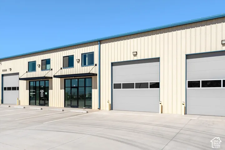 Corrugated metal siding with a blue trim roofline, multiple glass storefront entries with awnings, and large roll-up garage doors with window panels