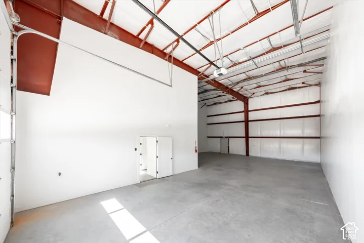 Concrete flooring, exposed structural beams, high ceilings, large roll-up door, and interior access doors
