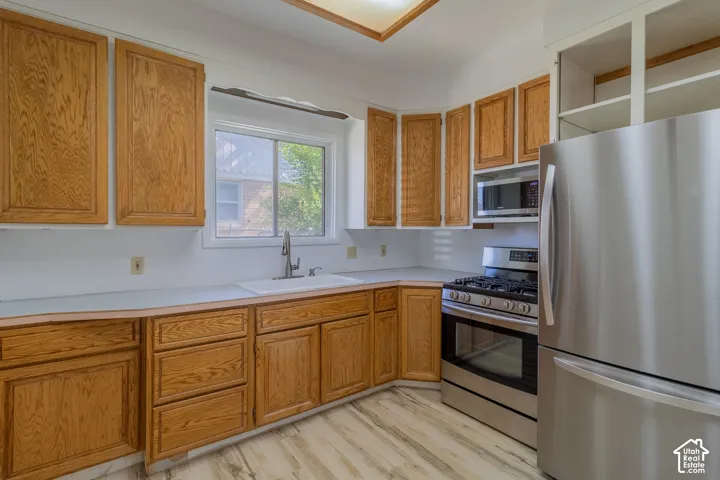 Kitchen featuring extensive wood cabinetry, light-toned countertops, a stainless steel gas range, an over-the-range microwave, and a stainless steel refrigerator