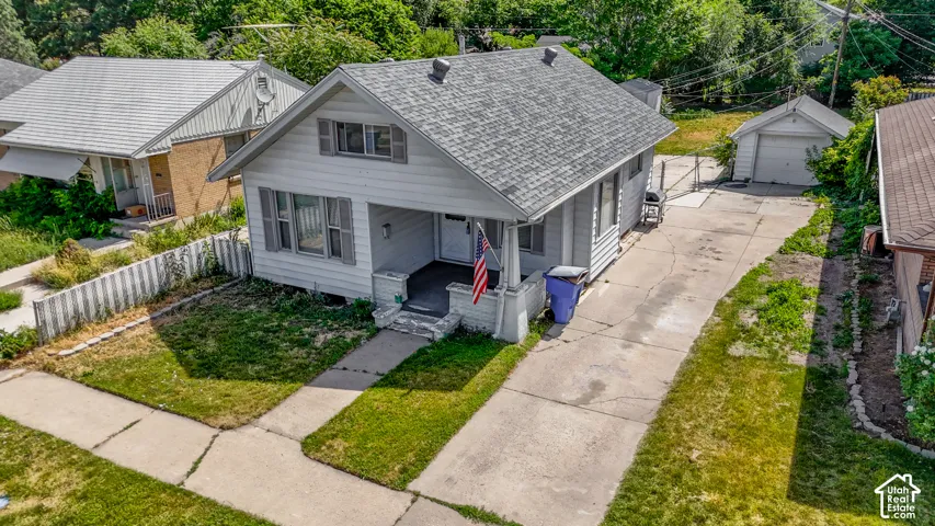 White siding exterior with a covered front porch, gray roof, and a detached garage with a concrete driveway