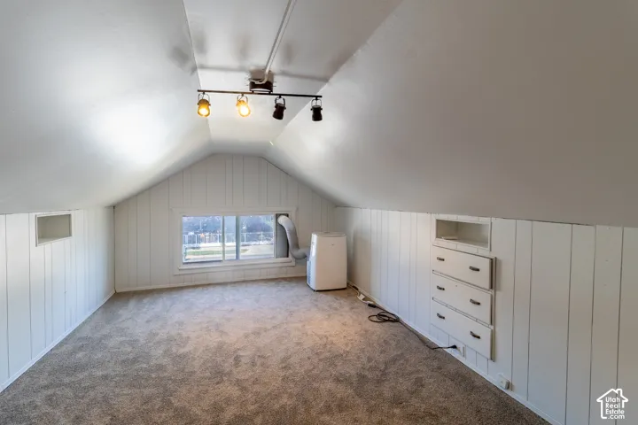 Sloped ceilings with track lighting, wall paneling, built-in drawer storage, and a single window