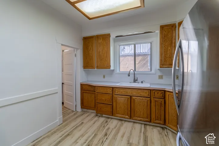 Wood-finish flooring, wood cabinetry, white countertops, built-in sink, and stainless steel refrigerator