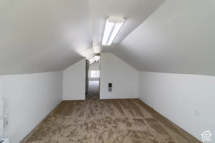 Attic space featuring sloped ceilings, recessed wall panels, and light brown carpeting