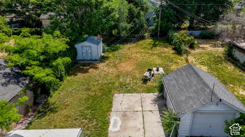 Expansive backyard oasis featuring a manicured lawn, mature landscaping with established trees, detached storage shed, concrete driveway, and attached garage with asphalt shingle roofing