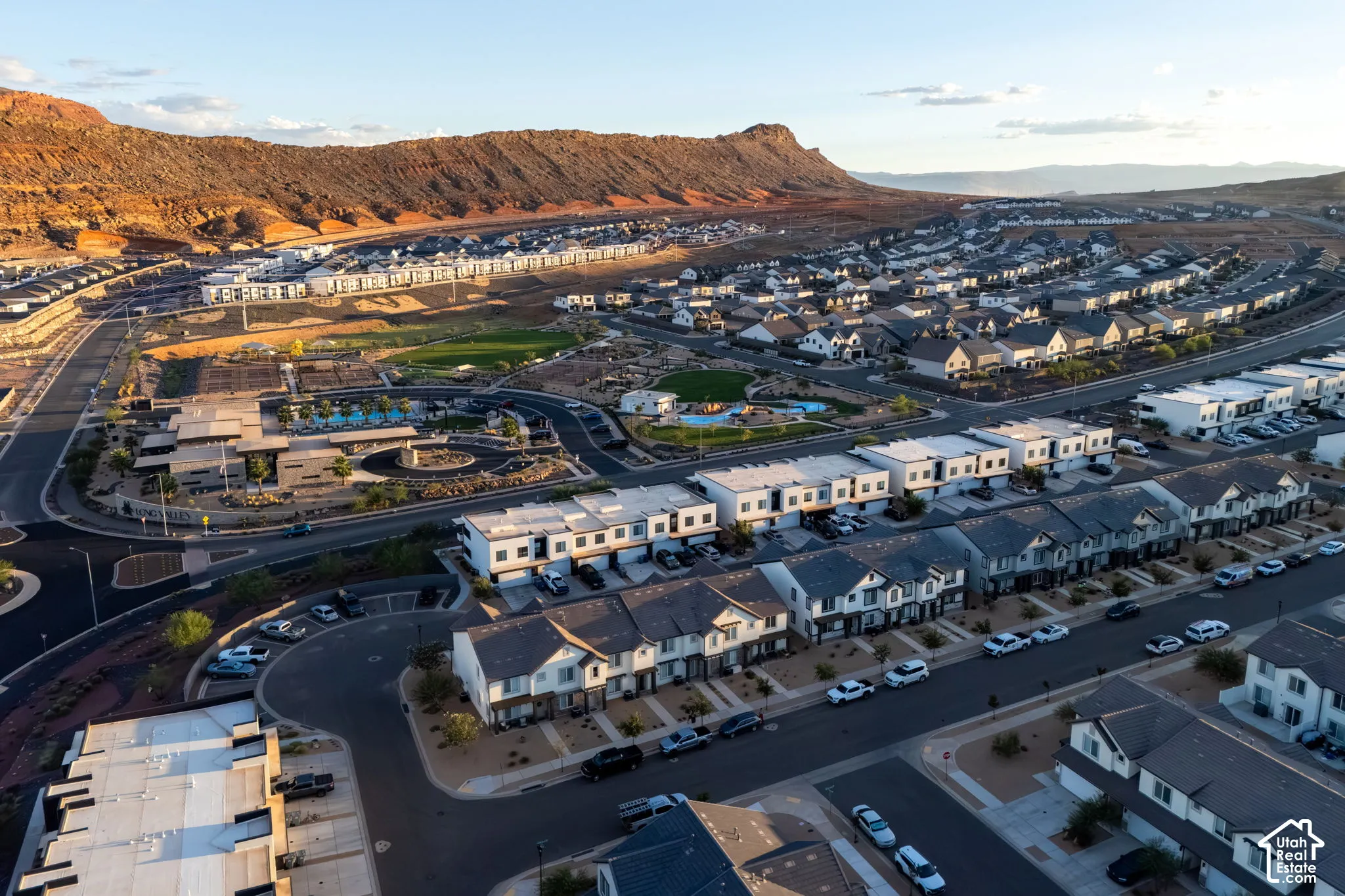 Expansive residential development with contemporary architectural styles, a community pool, and manicured green spaces, all set against a prominent mountainous backdrop