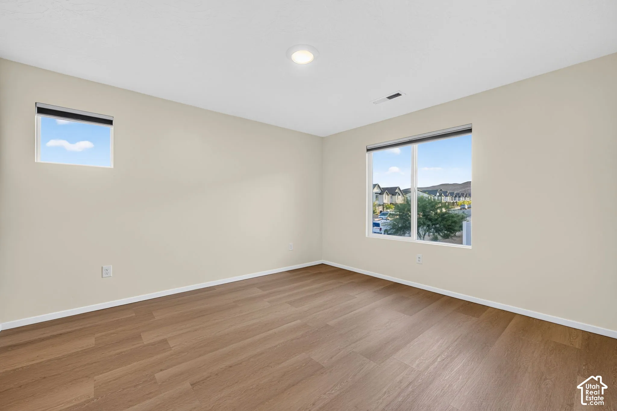 Wood-finish flooring with light-toned walls, featuring a large window and an additional smaller window