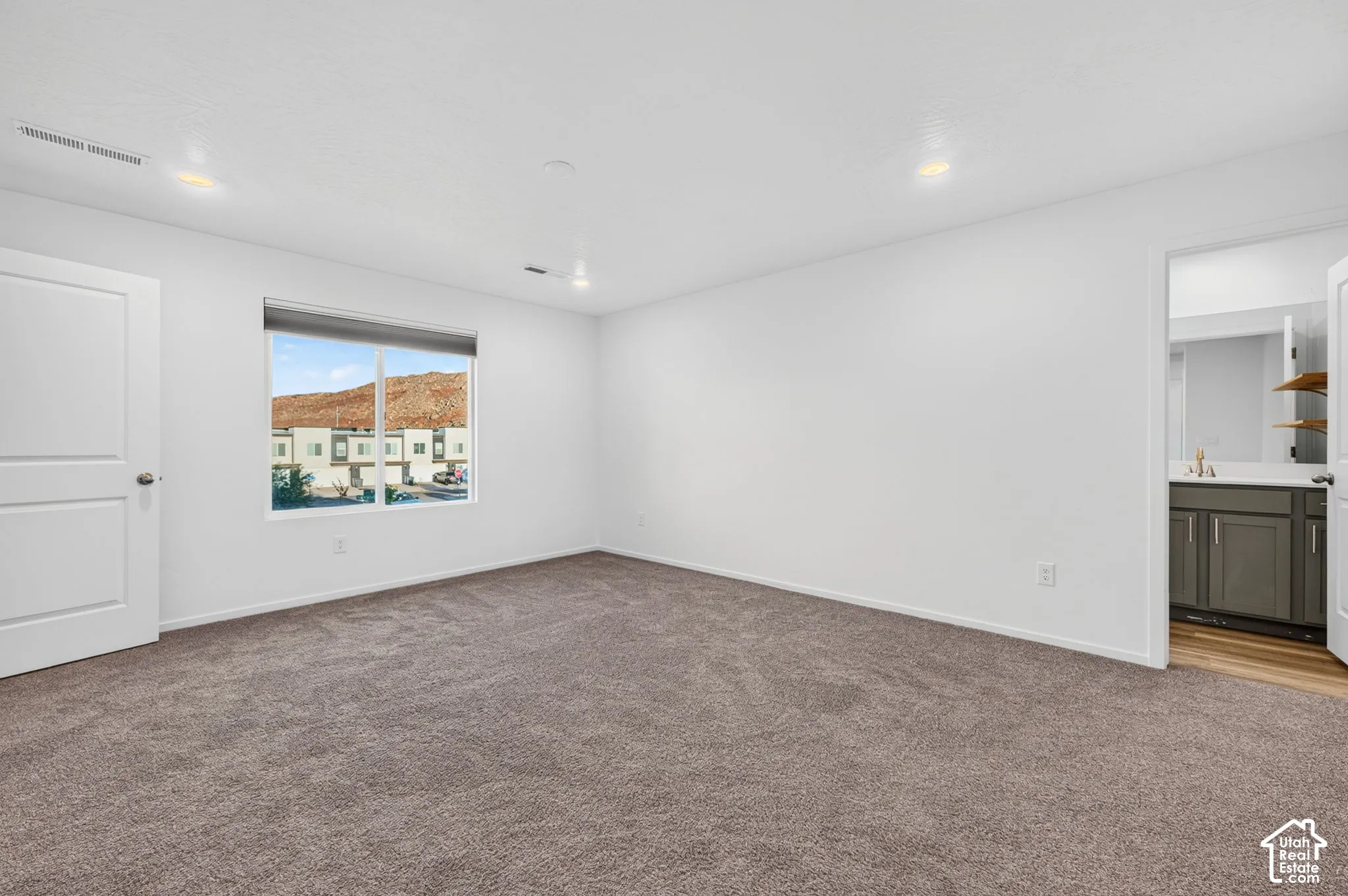 Spacious room with plush carpet flooring, recessed lighting, and a white interior door