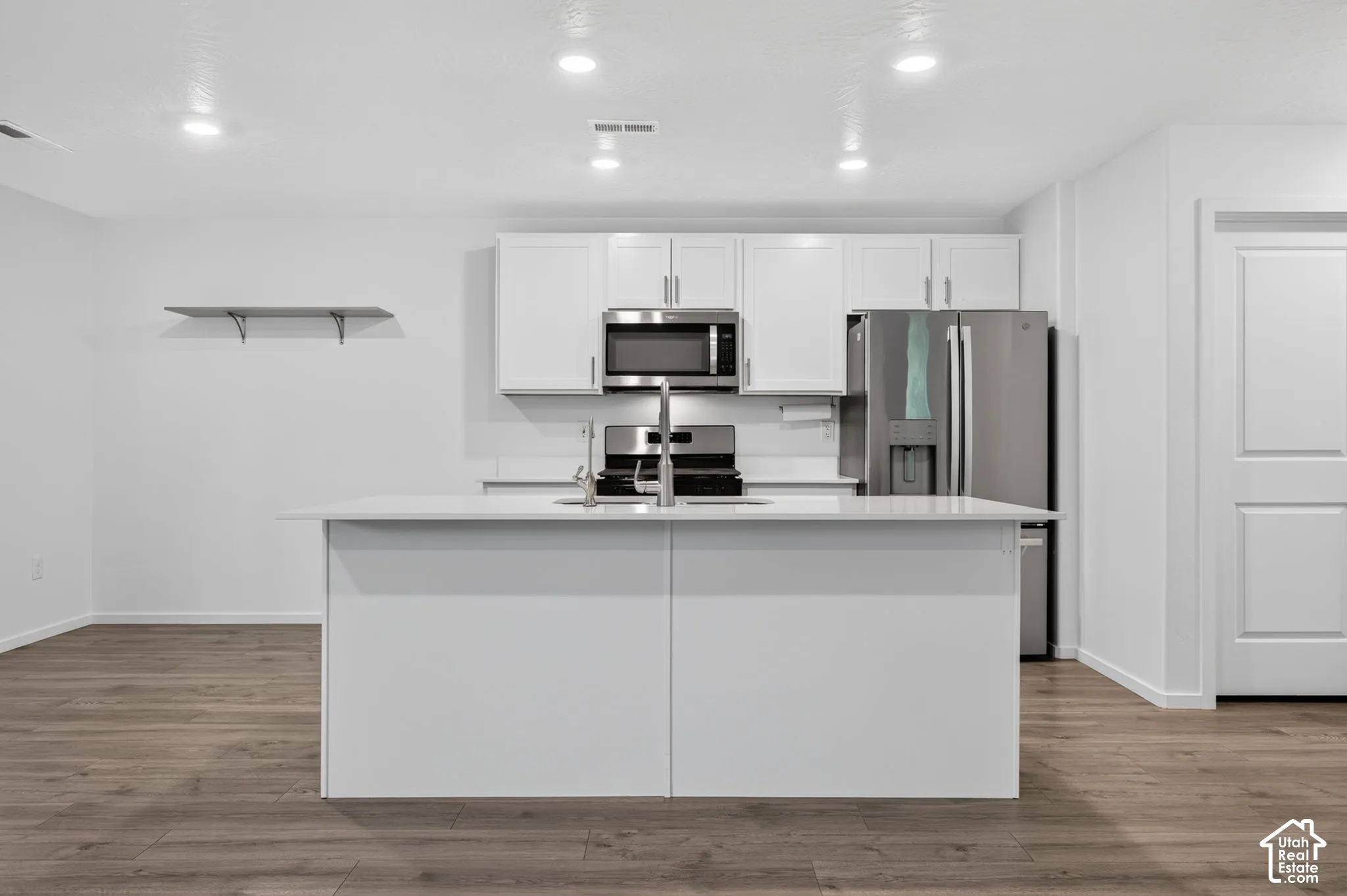 Kitchen featuring white cabinetry, stainless steel appliances, a center island with sink, and wood-finish flooring