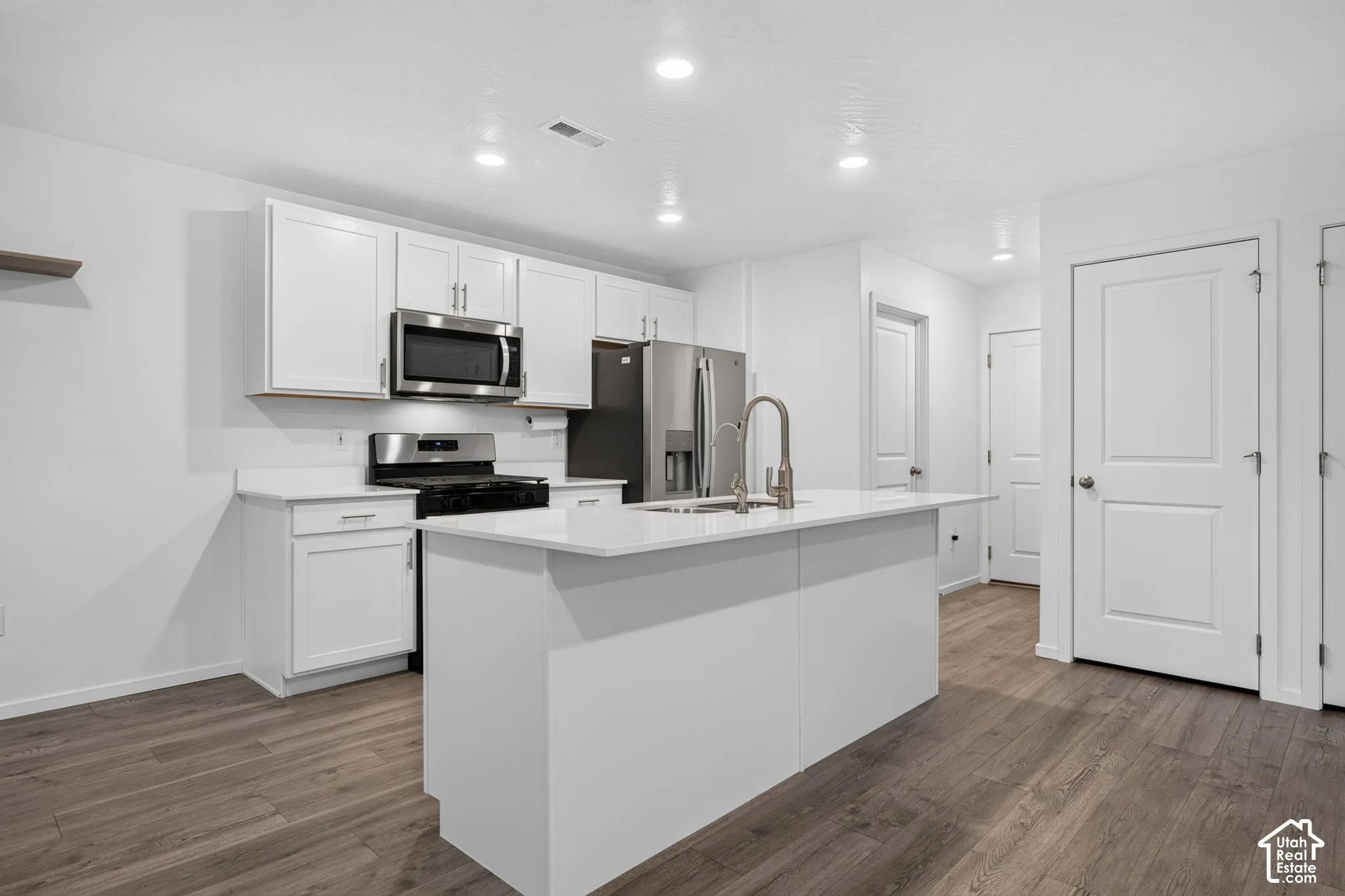 Kitchen featuring white cabinetry, stainless steel appliances, a center island with sink, white countertops, and wood-finish flooring