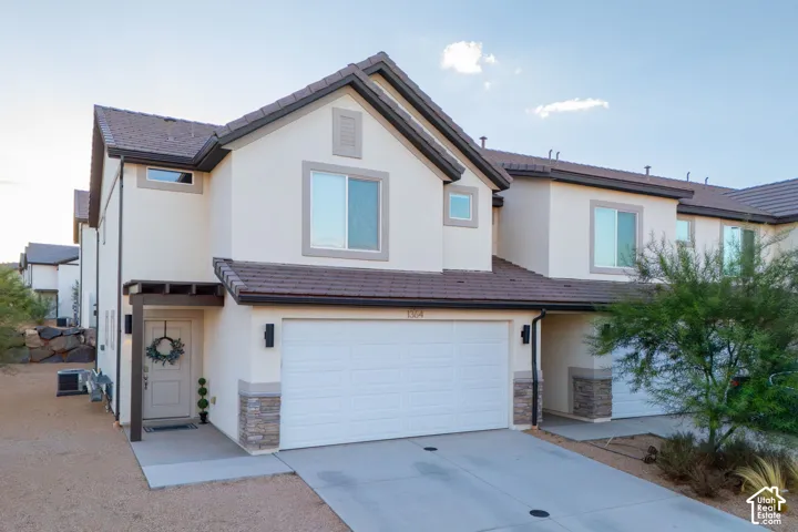 Stucco exterior with stone accents, attached garage, covered entry, and dark tile roofing
