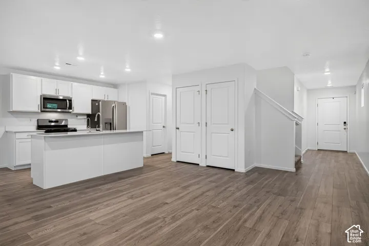 Open-concept living space with wood-finish flooring, white cabinetry, stainless steel appliances, and an island with a sink